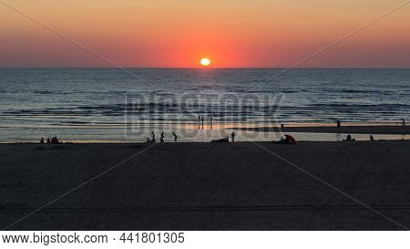 People On The Beach In The Reflektion Of The Sunset On The Dutch North Sea Coast. A Summer Scene.
