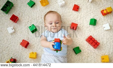 Cute Baby Boy Playing Toy Car On Carpet Next To Heap Of Colroful Toys, Blocks And Bricks. Concept Of