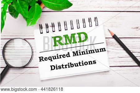 On A Light Wooden Background, A Magnifying Glass, A Pencil, A Green Plant And A White Notebook With 