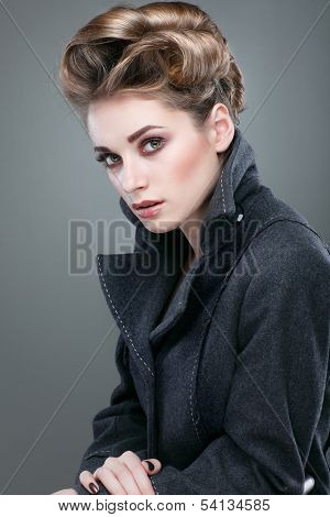 Portrait of elegant young woman in a grey overcoat  on a grey background