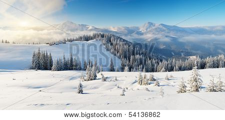 Winter landscape on a sunny morning in the mountains. The cabins of shepherds on the hill. Carpathians, Ukraine, Europe. View of the ridge of the mountain Chornohora from Kukul