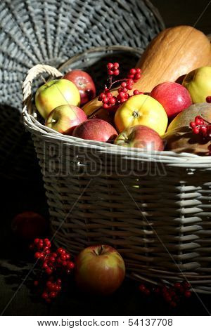 Juicy apples and pumpkin in wooden basket on table close-up