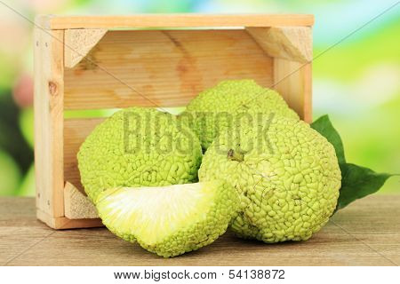 Osage Orange fruits (Maclura pomifera) in crate, on wooden table, on nature background