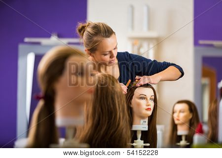 Pretty female hairdresser/haidressing apprentice/student training on an apprentice head