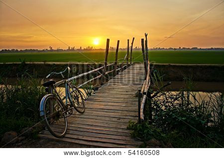 Bicycle On Wooden Fence Of Bridge At Sunset