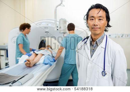 Portrait of male radiologist with nurses preparing patient for CT scan test in hospital