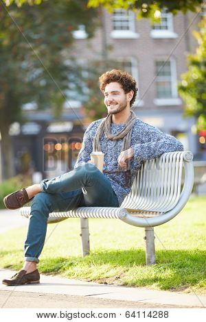Man Relaxing On Park Bench With Takeaway Coffee