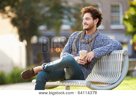 Man Relaxing On Park Bench With Takeaway Coffee