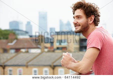 Young Man Relaxing On Roof Terrace With Cup Of Coffee