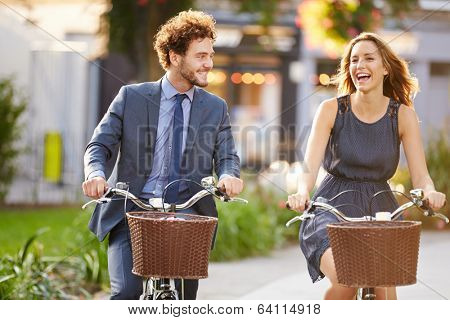 Businesswoman And Businessman Riding Bike Through City Park