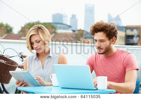 Couple On Roof Terrace Using Laptop And Digital Tablet