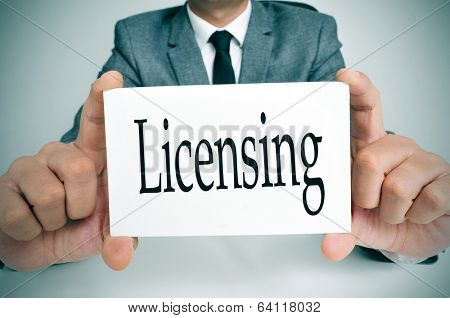 man wearing a suit sitting in a table showing a signboard with the text licensing written in it
