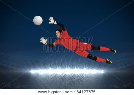 Fit goal keeper jumping up against large football stadium with spotlights under dark sky