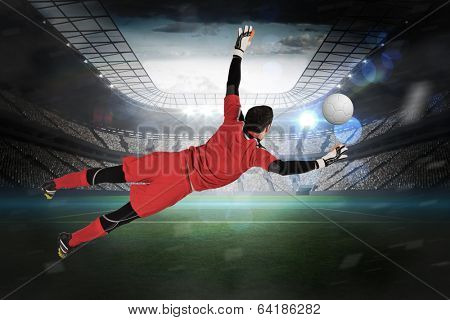 Fit goal keeper jumping up in a large football stadium with lights
