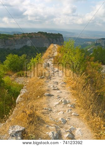 Pathway and precipice in mountains, cloudy sky