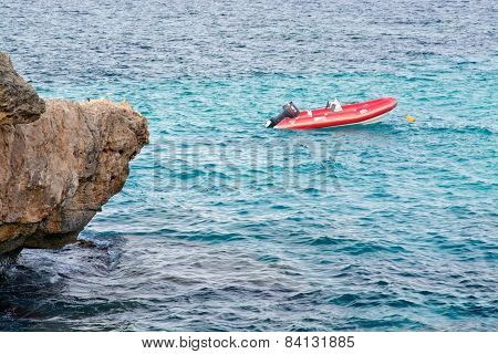 Small moored red lifeboat and rock