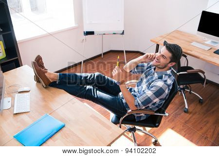 Happy relaxed businessman sitting on the office chair and talking on the phone in office