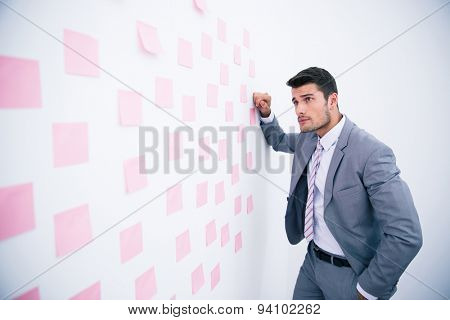 Handsome businessman looking on wall with stickers in office