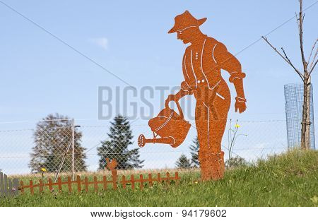 Gardeners Figure Pours Flowers. Rusty Garden Decoration