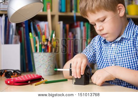 Portrait of cute school boy sitting at his desk and sharpening pencils. Child preparing for lessons.