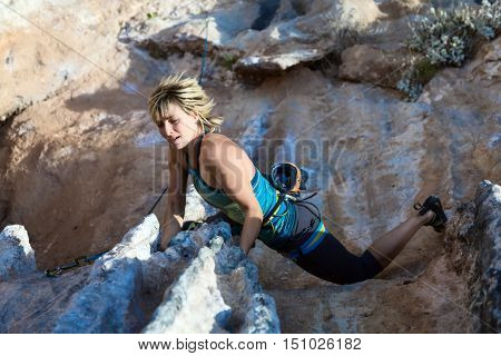 Female Athlete climbing natural rock keeping hold and hanging over deep abyss