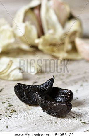 closeup of some black garlics on a rustic white wooden table and a garlic head in the background