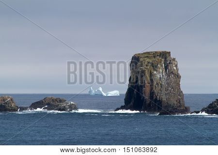 Atlantic coastline with large rocks and iceberg.