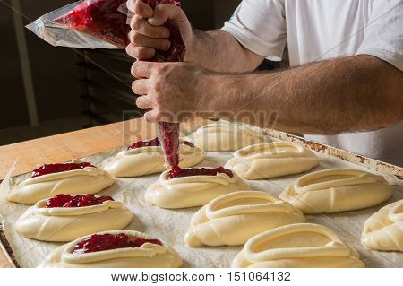 Raw sweet yeast dough on a baking sheet filling buns jam. Preparation for baking. The concept of chefs and baking.