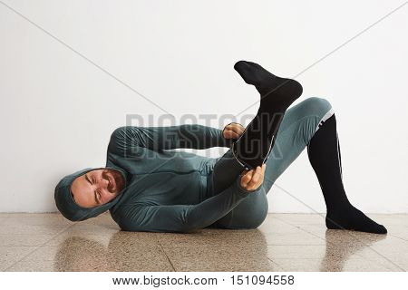 Funny fitted male athlete in winter thermal suite smiling and dressing up his long snowboard socks on floor
