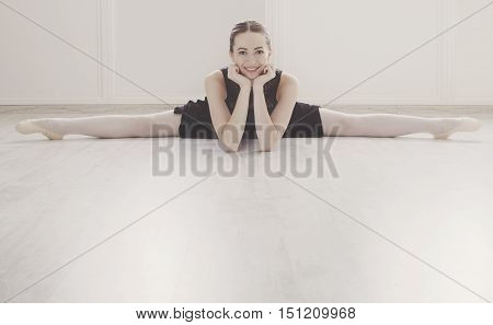 Classical Ballet dancer portrait. Beautiful graceful ballerine in black practice split ballet position in class room background. Ballet class training, high-key soft toning.