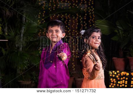 indian cute Boy and girl in traditional wear playing with sparklers or fulzadi or phuljhadi on diwali night