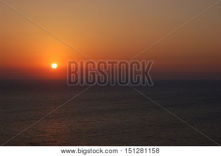 Orange sunset above the calm sea with little boat in the center