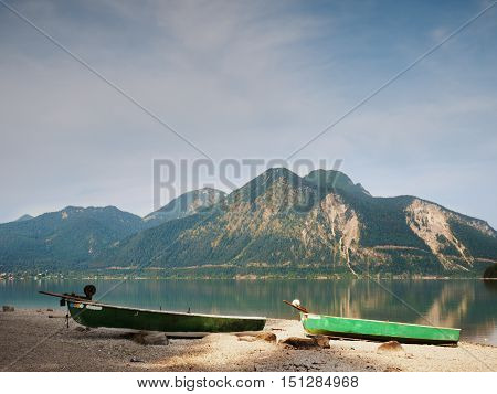 Abandoned Fishing Paddle Boat On Bank Of Alps Lake. Morning Lake Glowing By Sunlight.