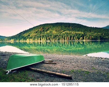 Abandoned Fishing Paddle Boat On Bank Of Alps Lake. Morning Lake Glowing By Sunlight.