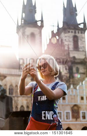 Beautiful young female traveler making self photo on her mobile phone on the background of the Church of Virgin Mary in Old Town Square in Prague. Kostel Panny Marie pred Tynem.