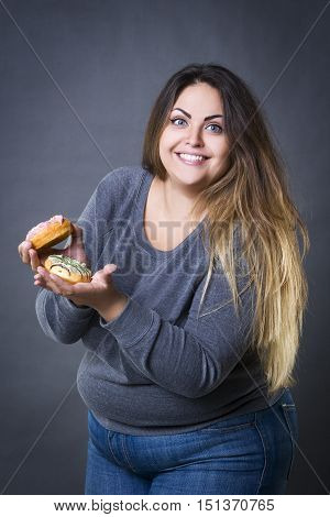 Happy beautiful young caucasian plus size model posing with donuts on a gray studio background fast food and unhealthy nutrition concept
