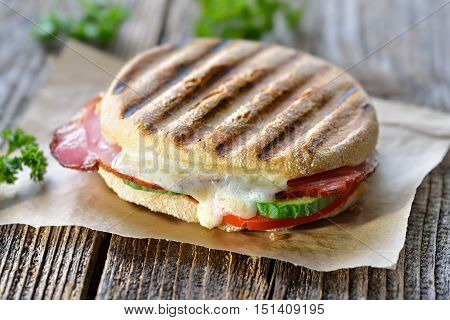 Grilled and pressed panini with smoked ham, cheese, cucumber and tomato served on sandwich paper on a wooden table