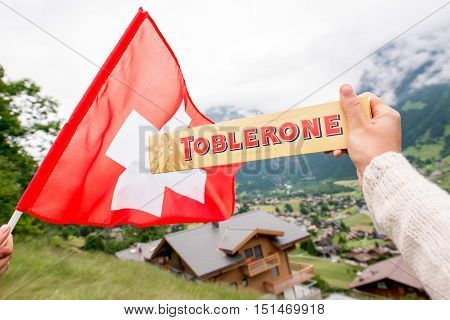 Grindelwald, Switzerland - June 26, 2016 Female hand holds Toblerone chocolate with swiss flag on the mountains background in Switzerland. Toblerone is a famous Swiss chocolate bar brand