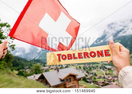 Grindelwald, Switzerland - June 26, 2016 Female hand holds Toblerone chocolate with swiss flag on the mountains background in Switzerland. Toblerone is a famous Swiss chocolate bar brand