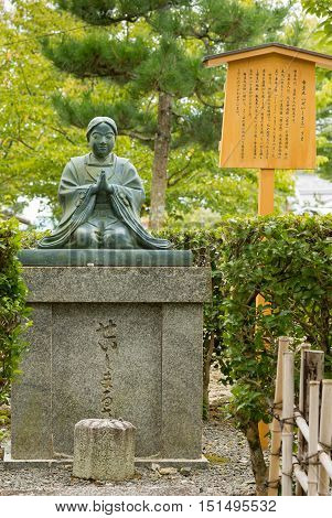 Kyoto Japan - September 15 2016: Kneeling Quan Yin statue at Kurodani Buddhist Temple. Green statue stands on top of stone pedestal. Background green trees and yellow sign.