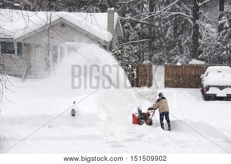 man removing snow on the driveway of the house by snow blower