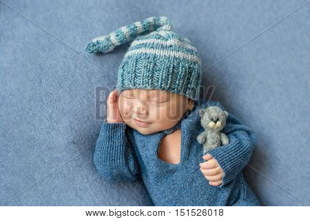 smilimg sleeping newborn boy in blue suit and hat with toy in hand