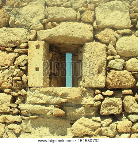 Window in old stone wall ruins of a medieval fortress on Crete Island, Greece. Square toned image