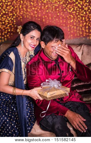 Indian wife surprising husband with a gift on diwali or anniversary or birthday, surprise gift concept and indian people or couple