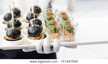 close up hand with white rubber glove holding plate with burger and seaweed for surve in banquet food business