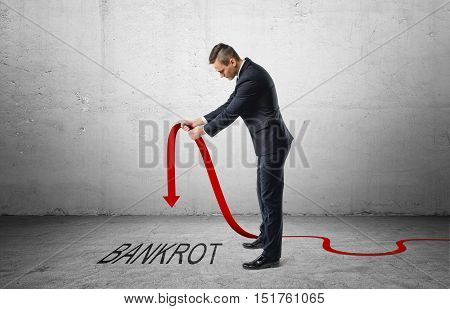 Businessman holding a red line graph with a downturned arrow which is pointing to the word 'bankrot'. Falling incomes. Losing profit. Bankruptcy and insolvency.