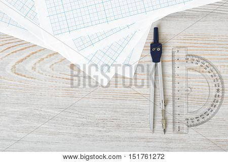 Layout with compass, protractor and graph paper on wooden surface in top view. Workplace of draftsman, architect, constructor or designer. Engineering work. Measurement. Tools for drawing.