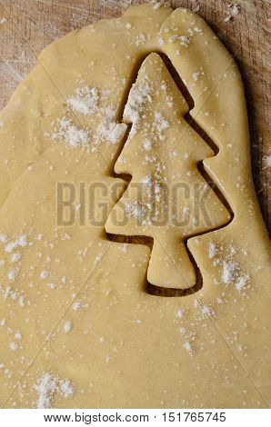 Christmas biscuit or cookie making concept with Xmas tree shape cut out of rolled dough. Flour sprinkles on pastry and wooden board beneath.