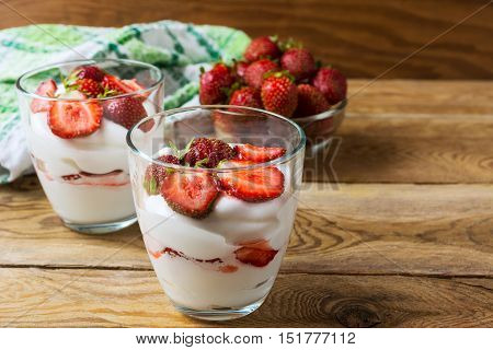 Summer dessert with whipped cream and strawberry on wooden background . Layered dessert with fresh ripe strawberry.