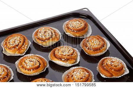 Cinnamon buns in tins of greaseproof paper on a baking tray on white.